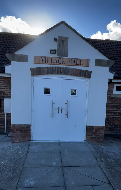 Rendered entrance gable at Earswick Village Hall with its sign, white double doors and retained brickwork.